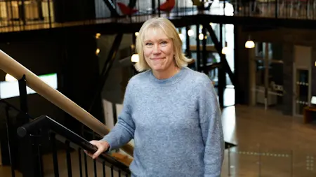 Helene Henriksson står med handen på ett trappräcke och tittar in i kameran.