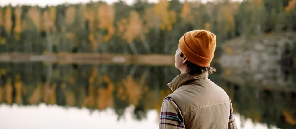 En person står med ryggen vänd mot kameran och blickar ut över en sjö och skog.