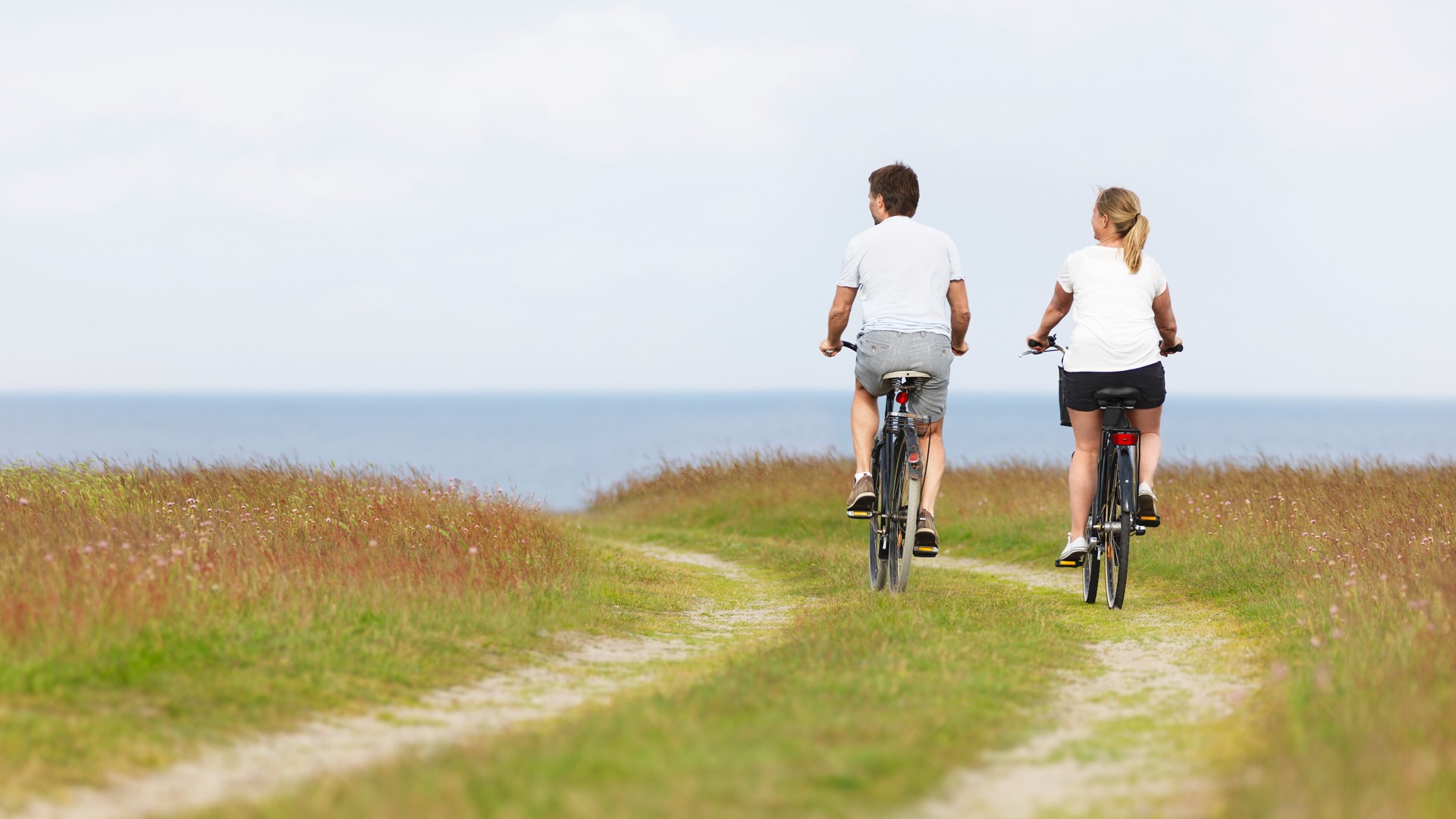 Kvinna och man cyklar på strand på väg till något. Känslan är hälsosamt lugn.