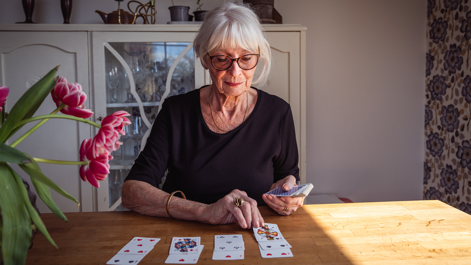 Äldre kvinnlig person lägger patients vid ett köksbord och ser nöjd ut.