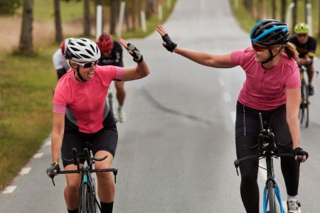 Två cyklande kvinnor med cykelhjälm gör high five.