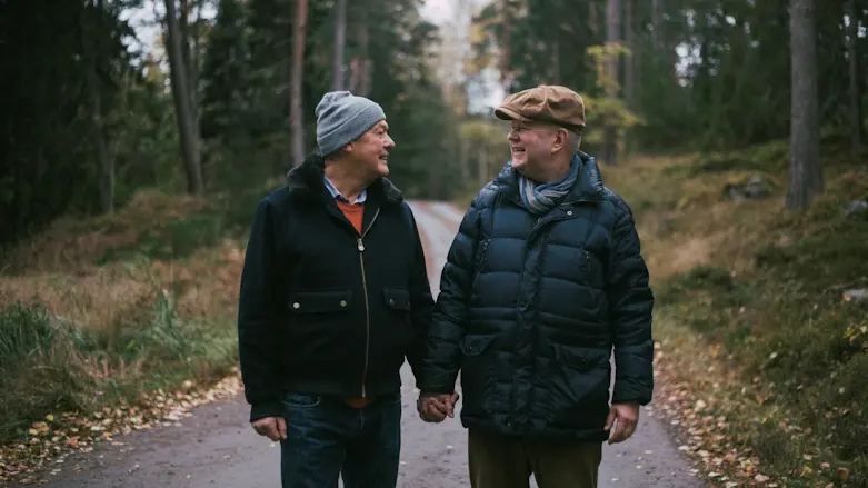 Ett äldre homosexuellt par håller varandra i handen under en skogspromenad
