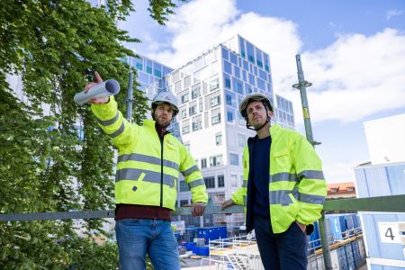 Två män i byggarbetskläder står framför Malmös nya sjukhusområde.