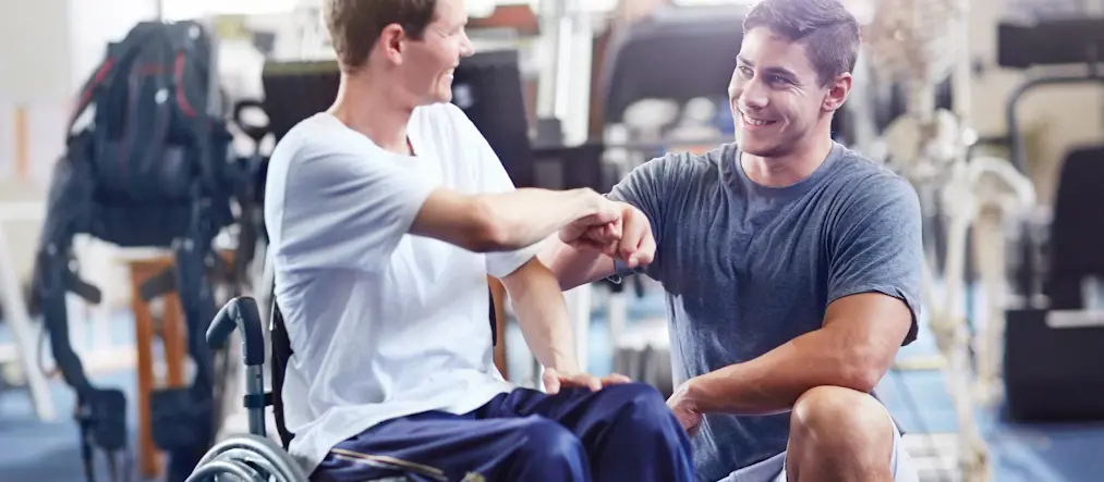 En man i rullstol gör en "fist-bump" med en annan man som står på knä bredvid mannen i rullstol.