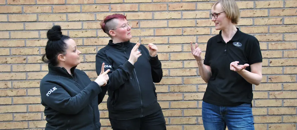 Tre personer talar teckenspråk med varandra.