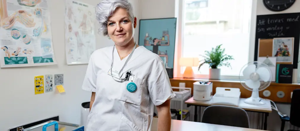 Catrin Knutsson, årets arbetsterapeut, iklädd vita vårdkläder, lutar sig mot ett skrivbord