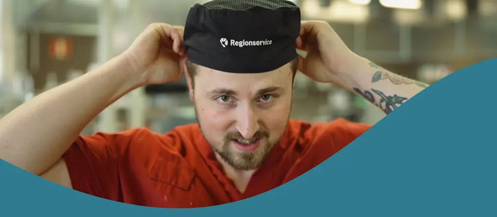 En manlig kock justerar sin kockmössa på huvudet.