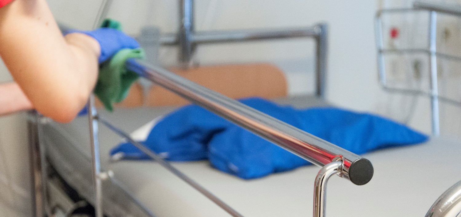 Närbild av hand som rengör sjukhussäng med en grön trasa.