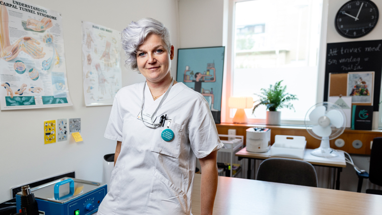 Catrin Knutsson, årets arbetsterapeut, iklädd vita vårdkläder, lutar sig mot ett skrivbord