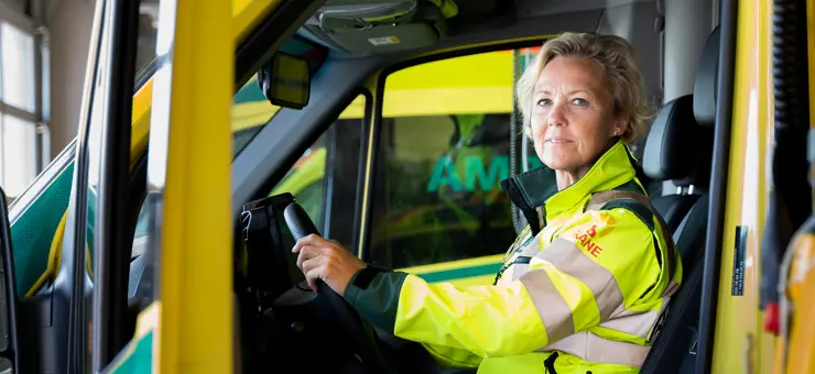 En kvinna sitter i arbetskläder vid ratten på en ambulans