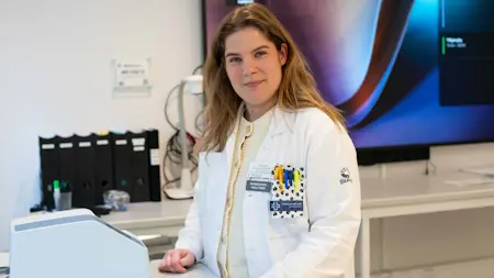 Amanda Gråberg, biomedicinsk analytiker, klädd i vita vårdkläder, står i ett labb, tittar in i kameran.
