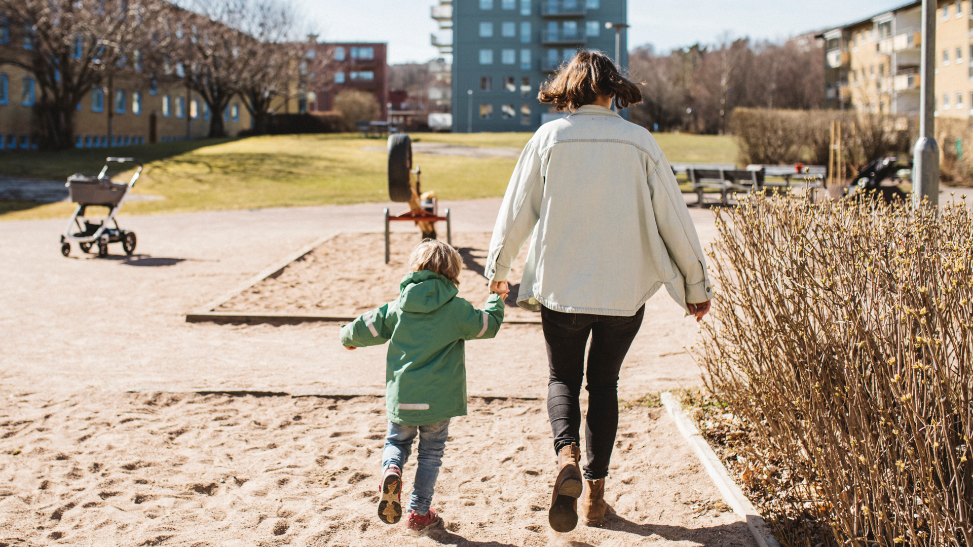 en mamma och ett litet barn går hand i hand över en innergård. Bilden tagen bakifrån.